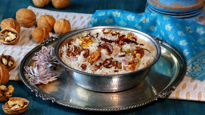 A side close up shot of ghee rice served in a silver bowl with shell flowers and walnuts in the background. A blue printed cloth is also seen - Kerala Ghee Rice with California Walnuts Recipe
